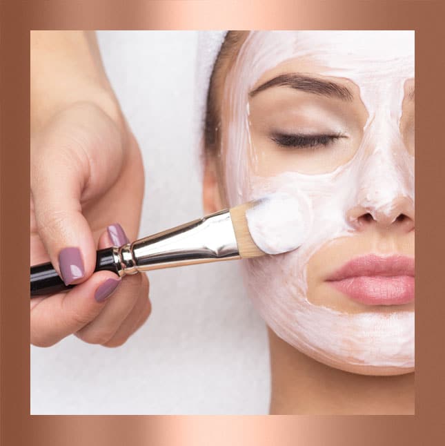 A woman receiving a facial mask treatment with a brush.